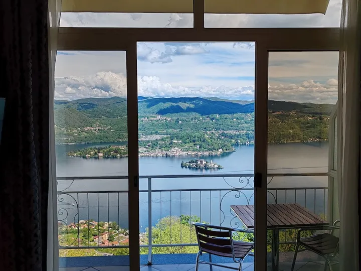 Vista sul Lago d'Orta e sull'Isola di San Giulio dalla porta-finestra di una camera con balcone, con tavolino e sedie